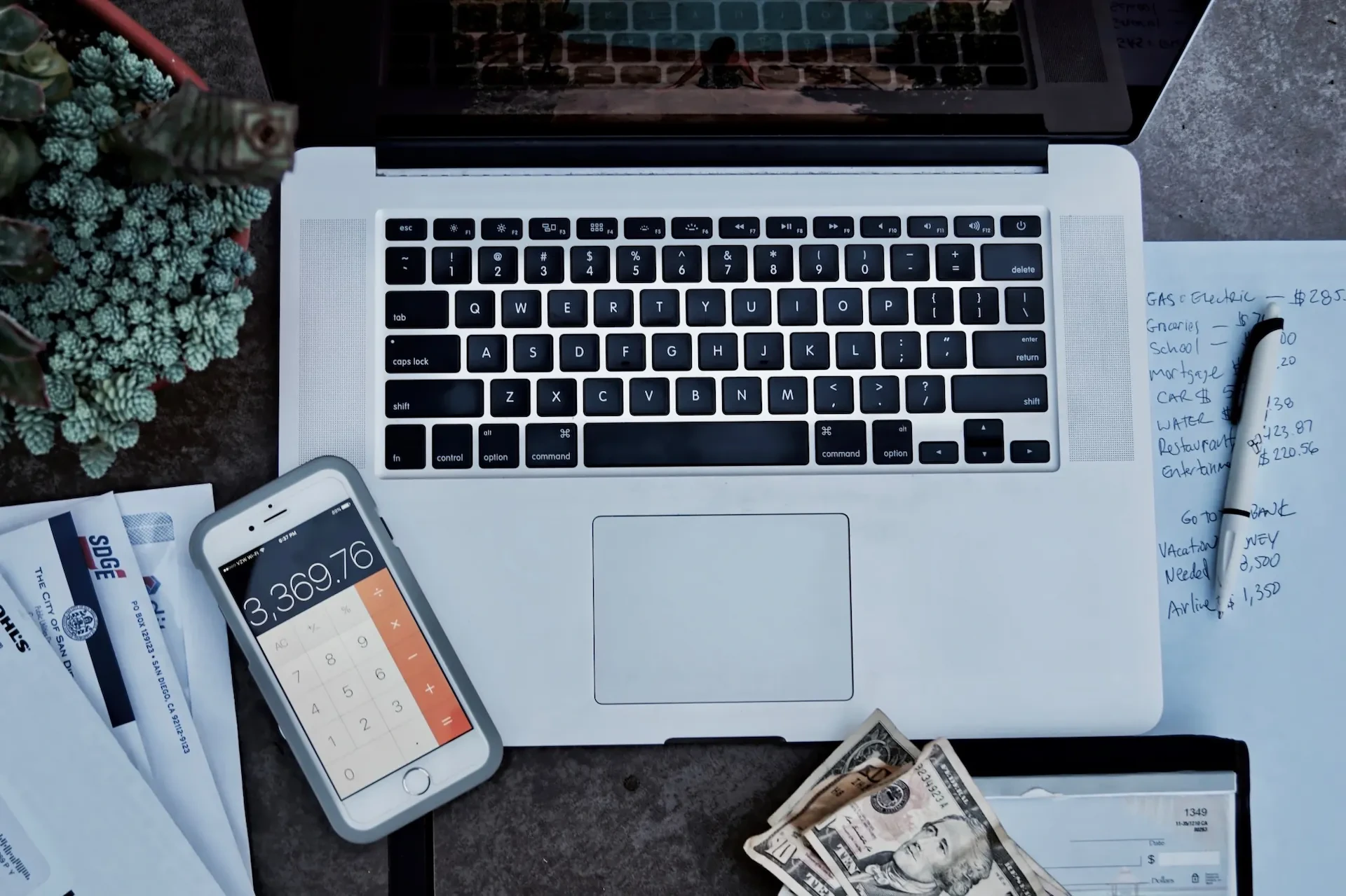 Laptop, phone, calculator, and cash on a desk.