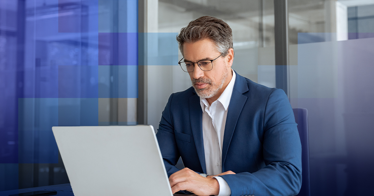 Man in a navy suit and glasses working on a laptop