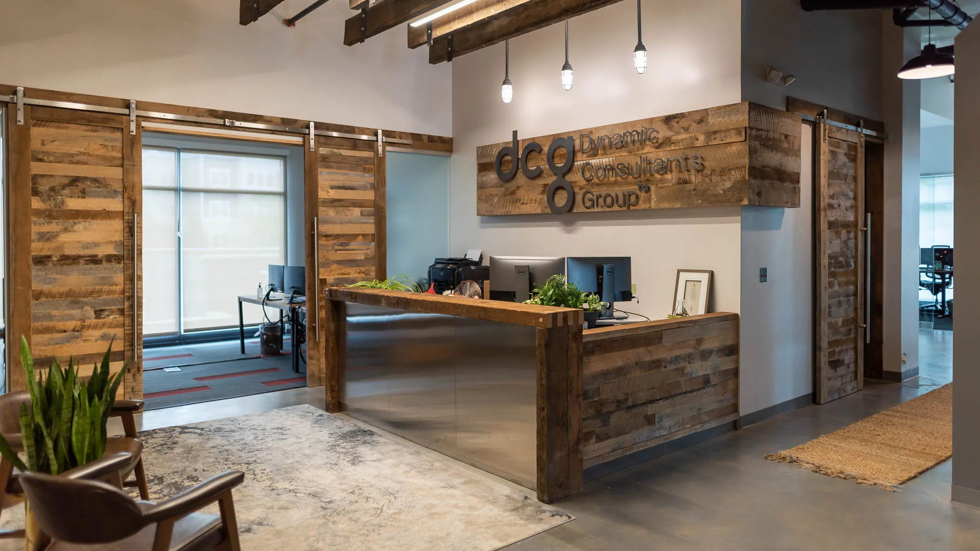 Modern office reception area with wooden accents and a sleek desk. Features plants and a logo for DCG Consultants Group.