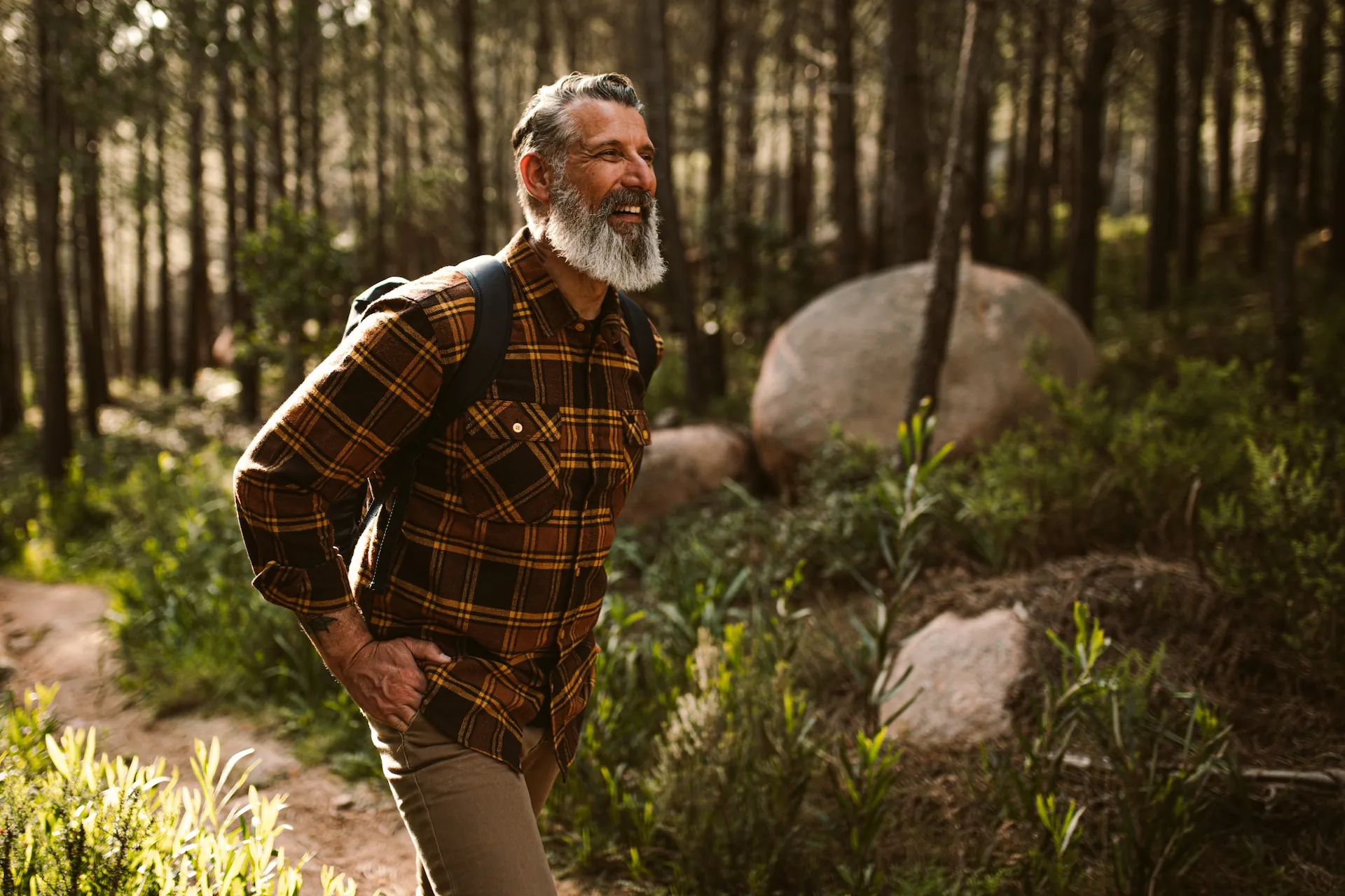 A smiling, bearded hiker pauses on a forest trail.