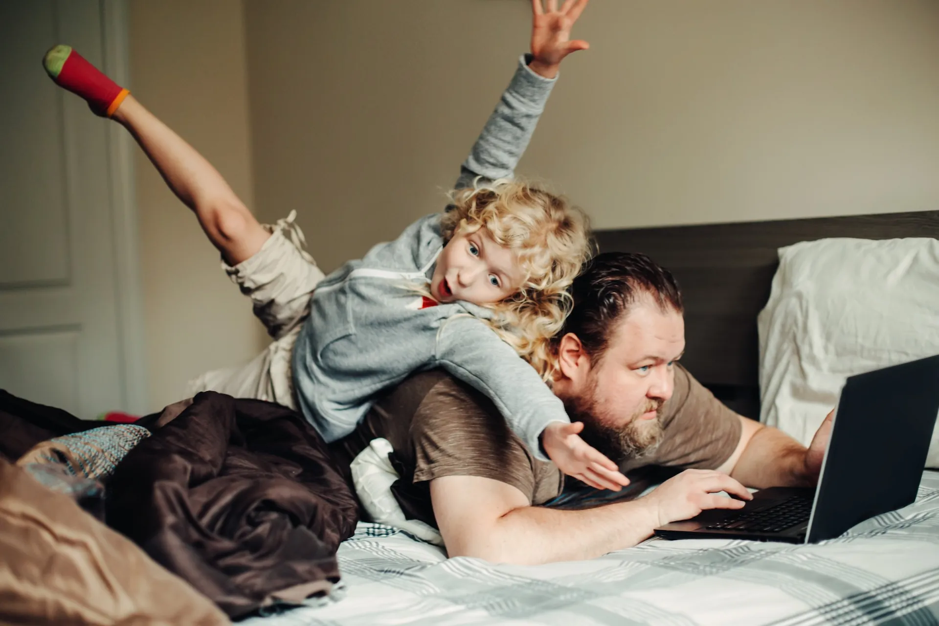 A child plays on a man's back as he uses a laptop at home.