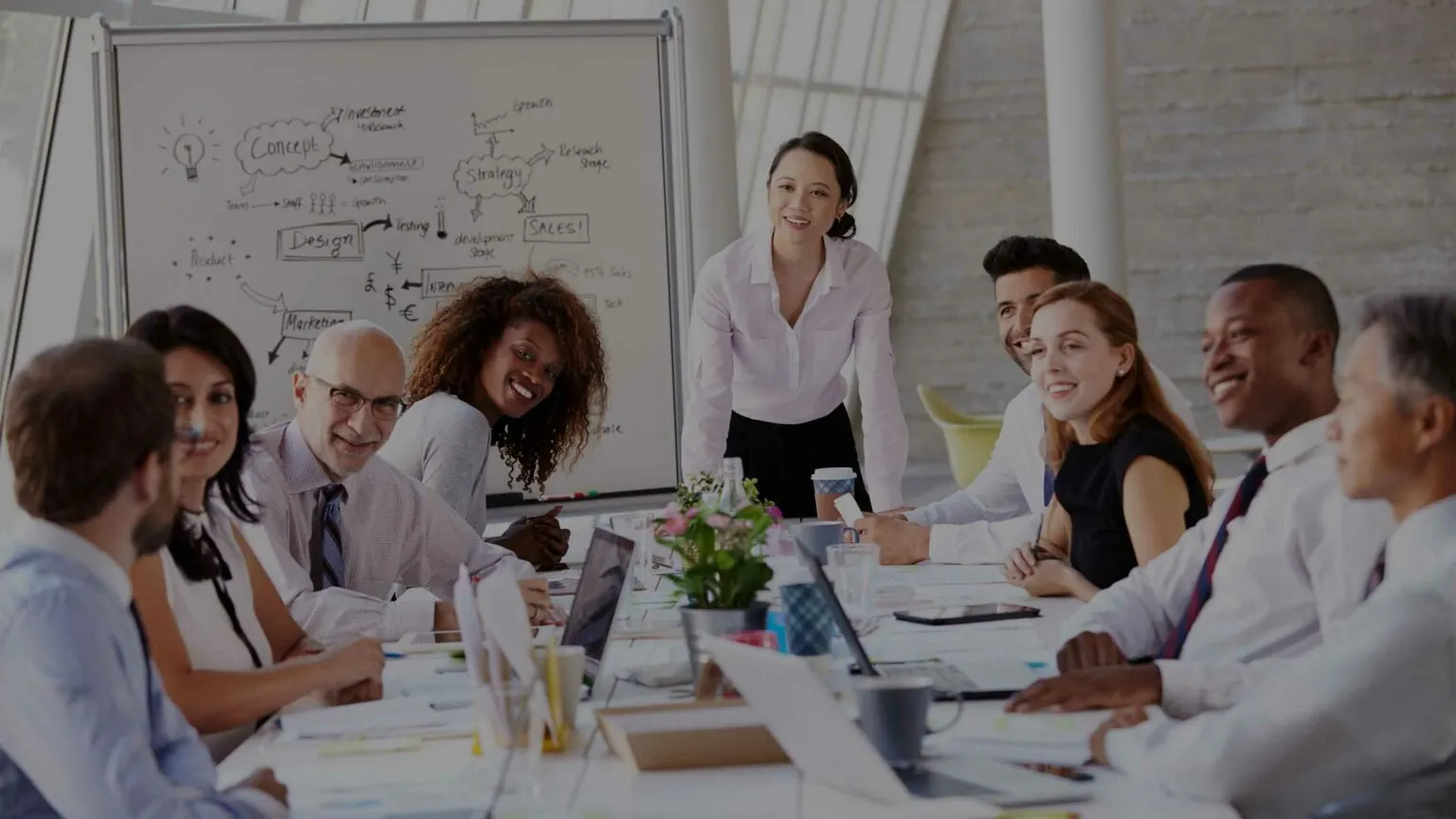 A diverse group of professionals engaged in a collaborative meeting around a conference table, with a whiteboard displaying ideas.