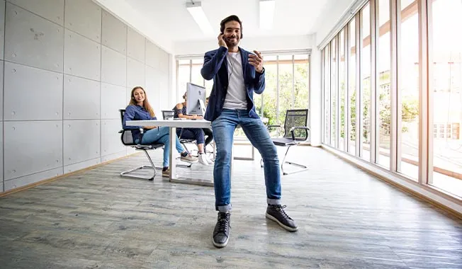 A modern office setting with three people engaged in a discussion. Bright natural light streams through large windows.