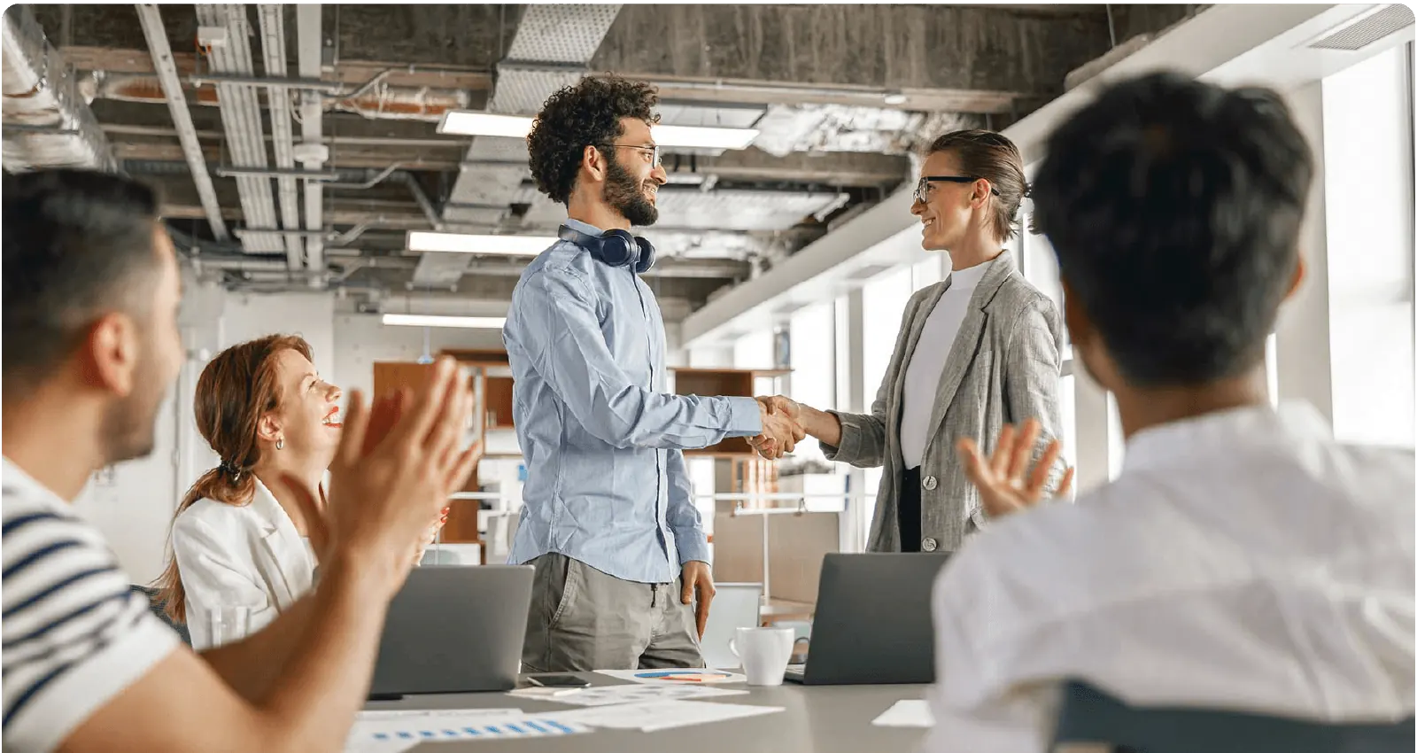 A professional meeting with participants applauding as two individuals shake hands, signifying agreement or success. Modern office setting.