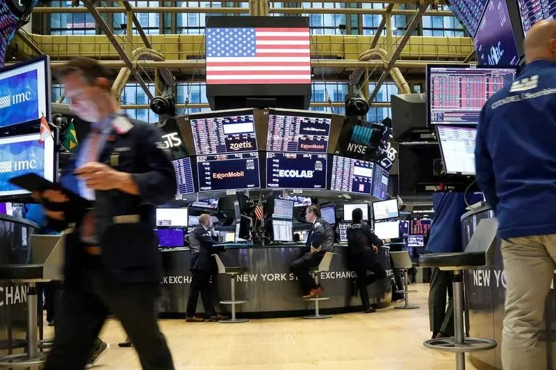 Traders actively work at the New York Stock Exchange with screens displaying stock prices and an American flag overhead.