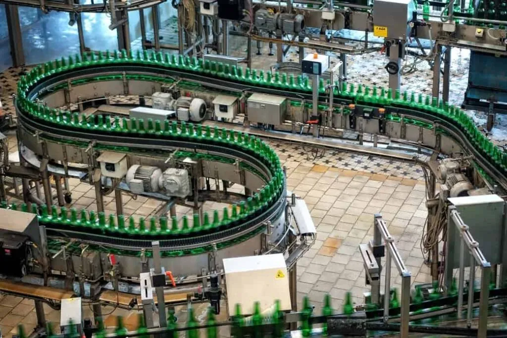 Aerial view of a bottling plant’s conveyor system with green glass bottles moving in a winding path amidst machinery.