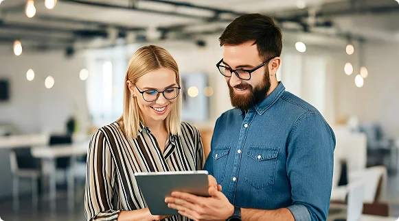 Two colleagues smiling as they review a tablet together in an open office.