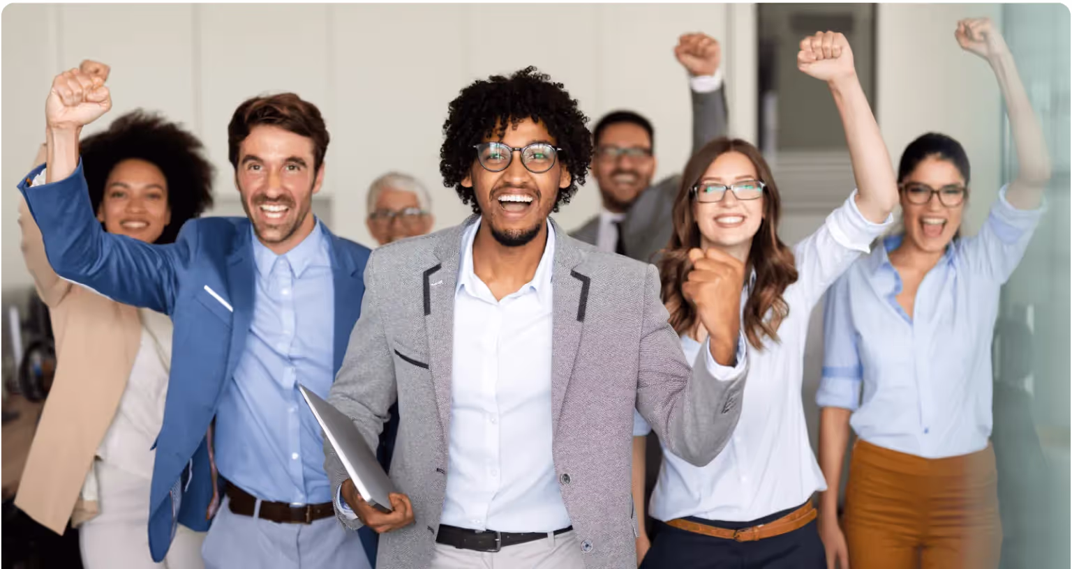 A group of colleagues walk forward together with their arms raised, celebrating.