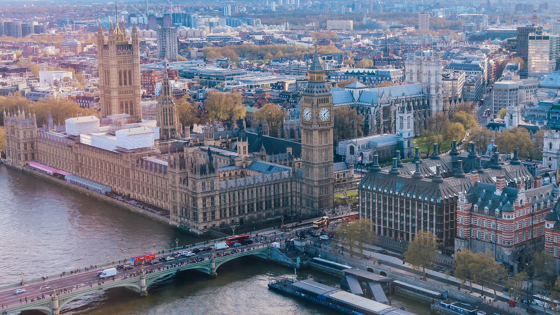 Aerial view of London's Houses of Parliament and Big Ben alongside the Thames, with bustling bridges and cityscape in the background.