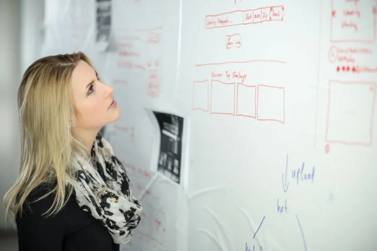 A person studying a glass whiteboard covered in a hand-drawn workflow in red and blue marker.